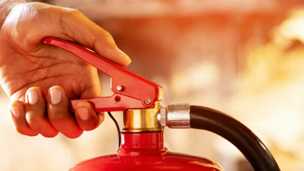 Hand am Feuerlöscher verdeutlicht die Wichtigkeit des Betrieblichen Brandschutzes