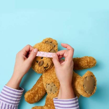 Kinderhände, die einen Teddybären mit einem bunten Motivpflaster verarztet