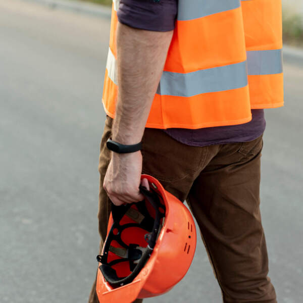 mann hat eine orangene warnweste an und hält in einer hand einen helm